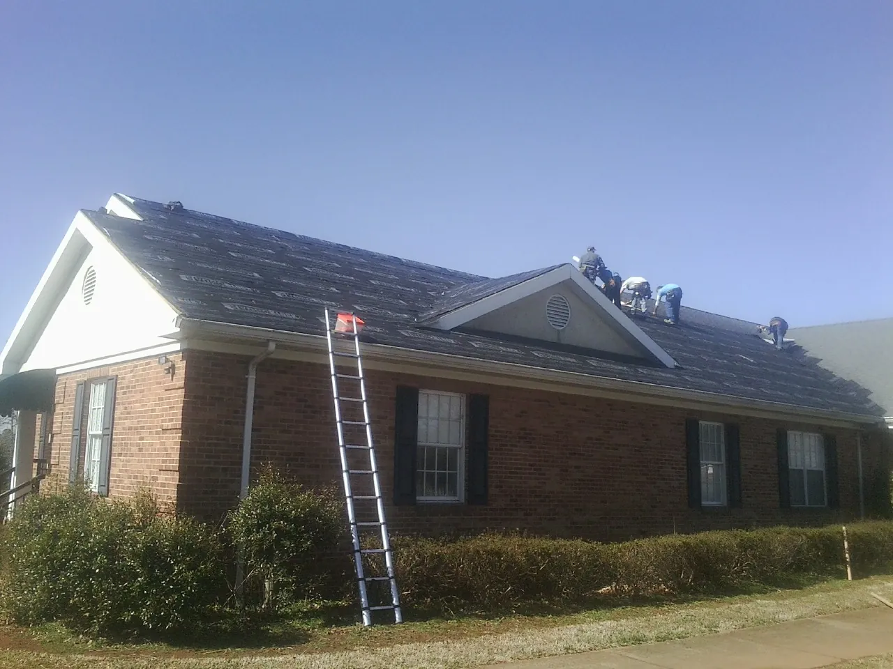 Crew tearing shingles off a brick ranch roof with a ladder set — Emergency Roof Repair work by our crew in Turbotville