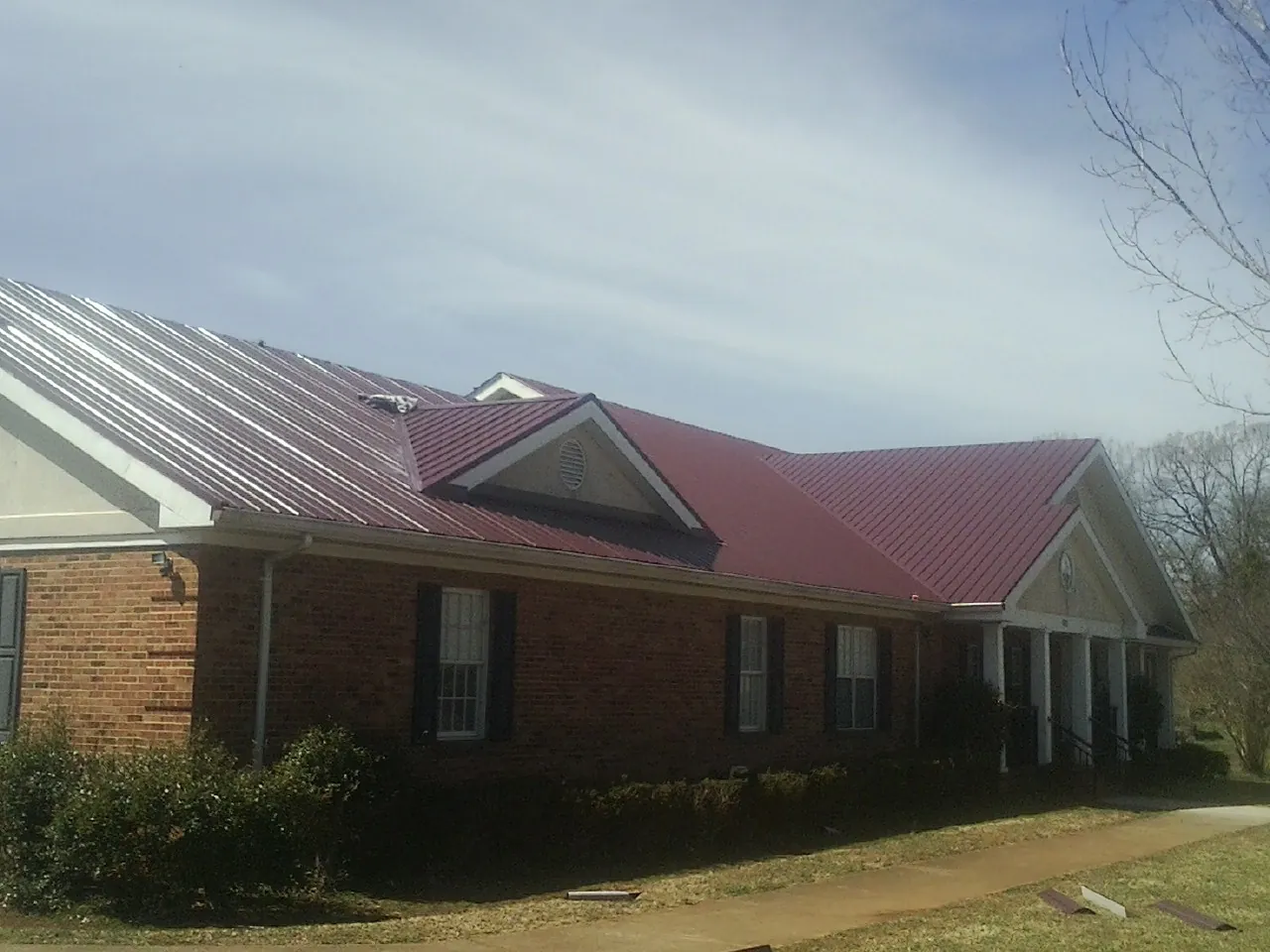 Red metal roof with gabled entries on a long brick building, from a Hail Damage Roof Repair job in Turbotville