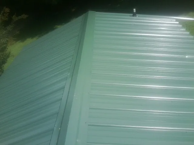 New green metal panels meeting at the ridge of a roof — Flat Roof Repair work by our crew in Turbotville