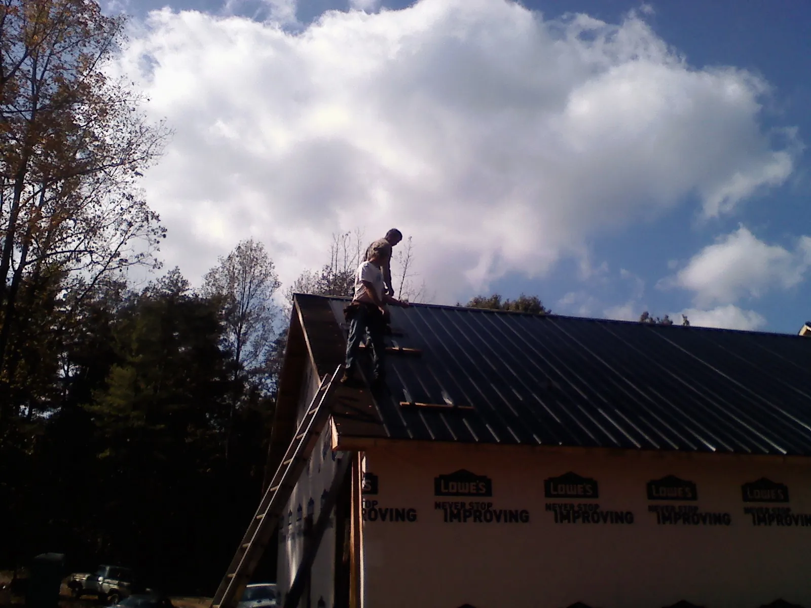 Roofer fastening dark metal panels high against a cloudy sky, from a Roof Inspection job in Turbotville
