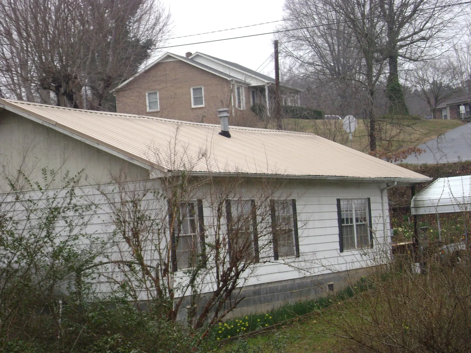 Tan metal roof on a white sided house set into a hillside — Commercial Roofing by Roofing Brothers in Turbotville
